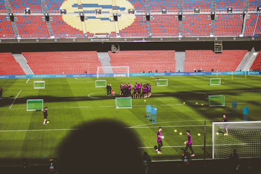 Football team training in a large empty stadium with vibrant red and blue seats.